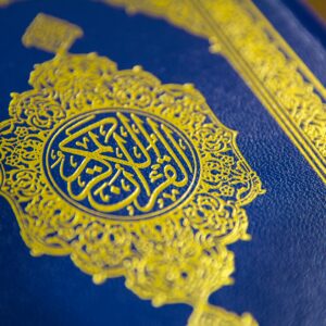 Close-up of intricate gold Quranic calligraphy on a blue cover, showcasing elegant Islamic design.